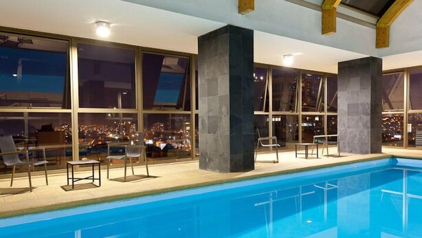 An indoor swimming pool with a city view, large windows, and modern architecture. - ECO PLAZA Santiago (Santiago)