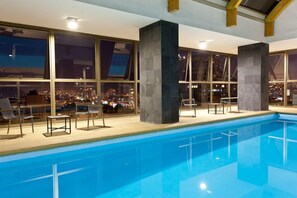 An indoor swimming pool with a city view, large windows, and modern architecture.