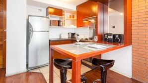 A modern kitchen with a refrigerator, microwave, and coffee maker. There are two bar stools and a dining table. - ECO PLAZA Santiago (Santiago)