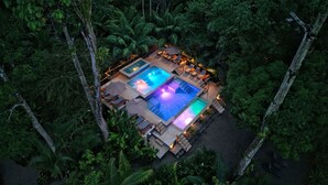 An aerial view of a resort with a swimming pool surrounded by lush greenery and trees.