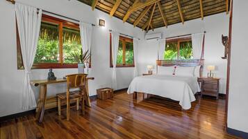 A bedroom with a wooden bed, a desk, and a chair. There are windows with curtains, an air conditioning unit, and a ceiling fan.