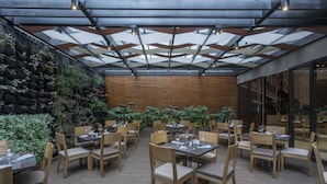 An indoor dining area with tables and chairs, a glass ceiling, and a wall with plants. - Mercure Bogotá Calle 100 (Bogotá)