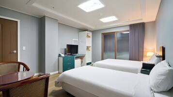 A hotel room with two beds, a desk with a computer, a TV, and a window with curtains.