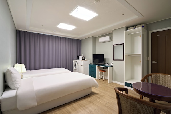 Habitación de hotel con cama, escritorio, silla, lavadora y televisor.