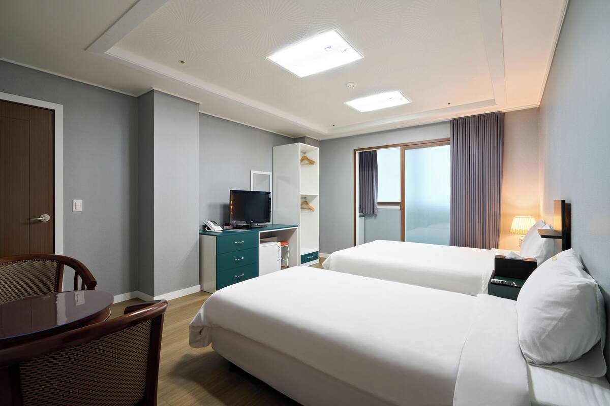 A hotel room with two beds, a desk, a chair, a TV, and a window with curtains.