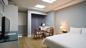 A hotel room with a bed, a desk with a computer, a washing machine, and a lamp.