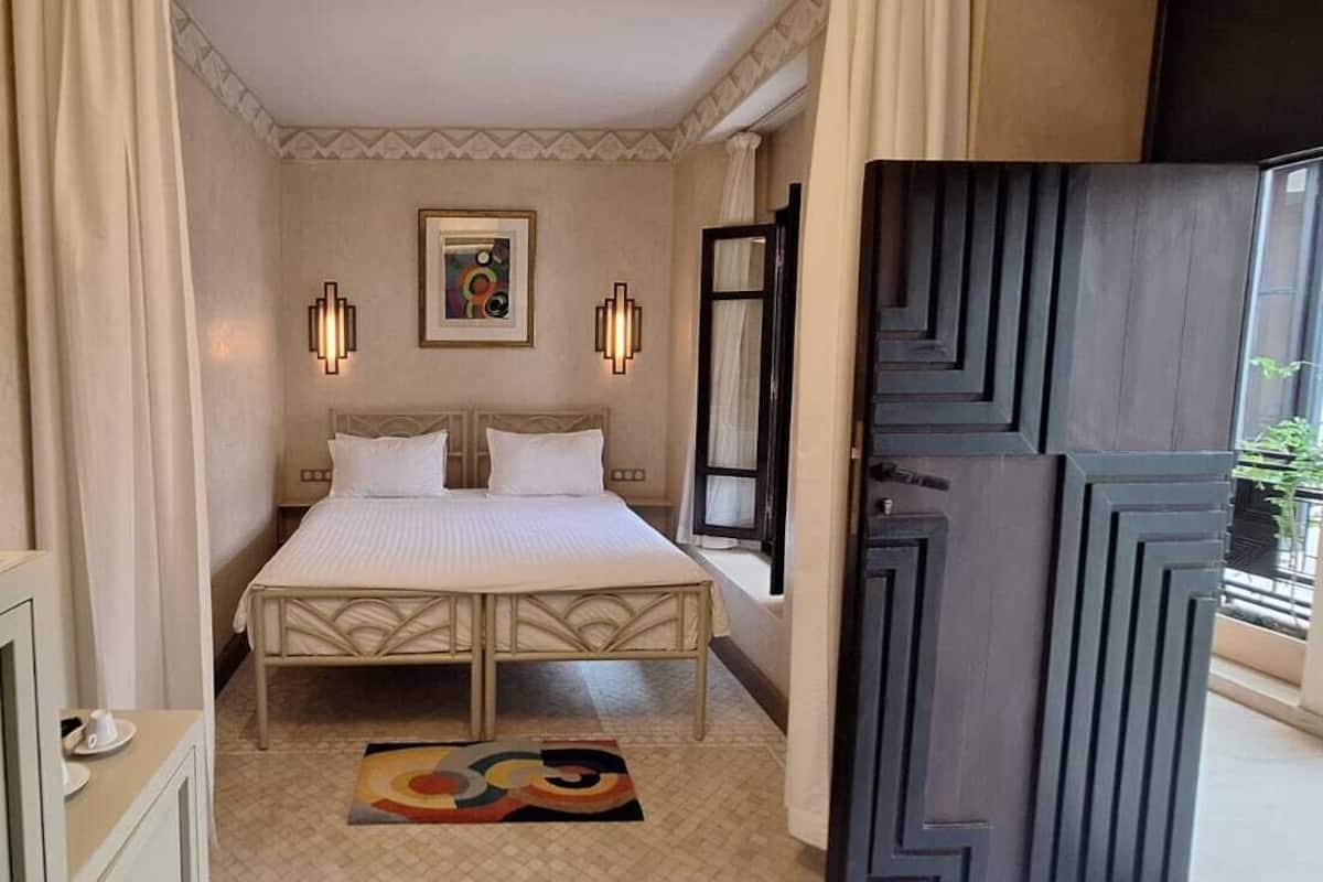 A hotel room with a bed, bedside lamps, a painting, and a view of the outdoors.