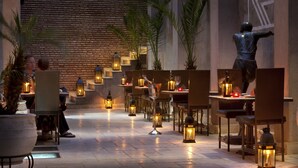 A restaurant with tables and chairs, illuminated by lanterns, and a statue in the background. - Villa Makassar (Marrakech)