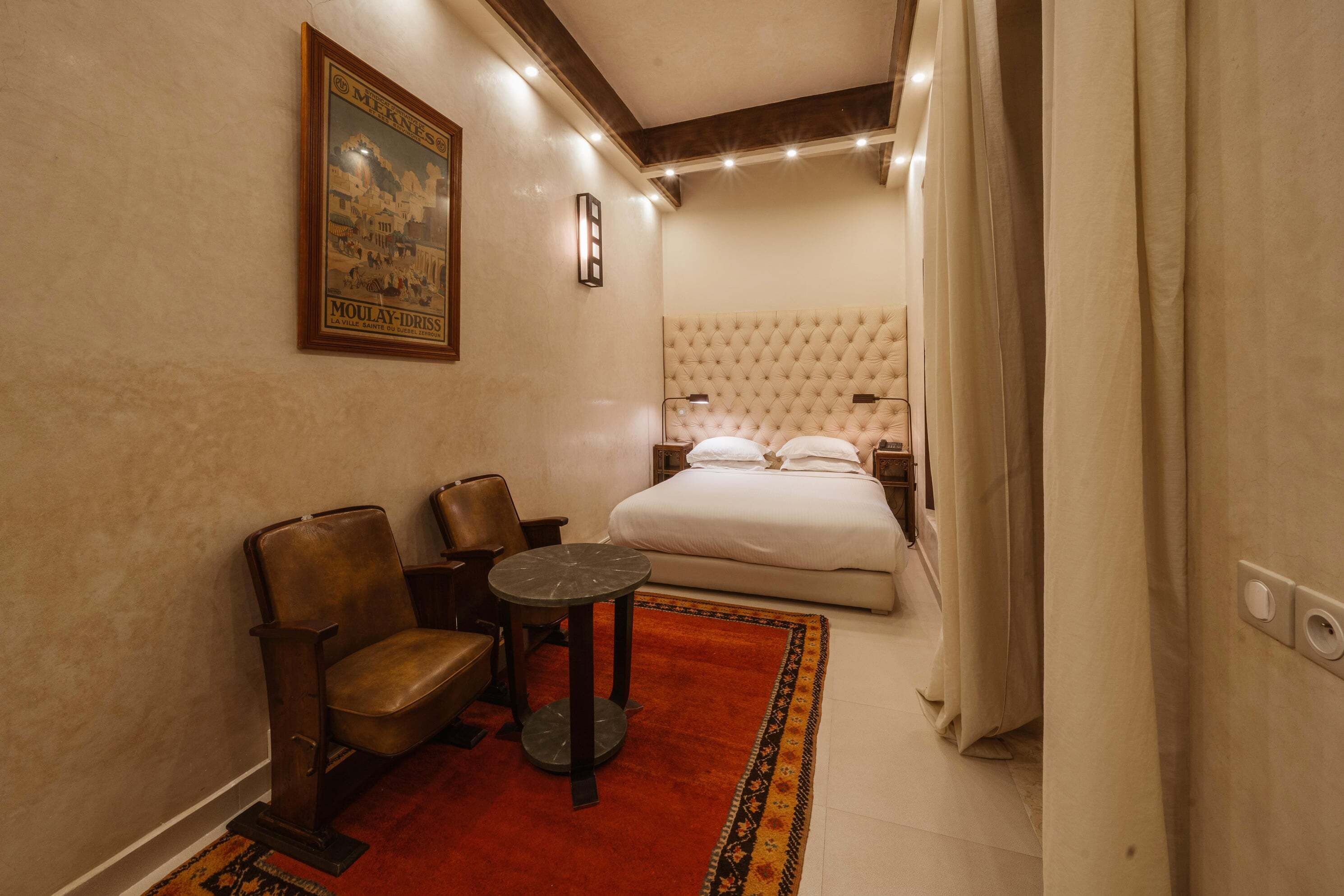 A hotel room with a bed, a seating area with chairs and a small table, a framed picture on the wall, and a red rug.