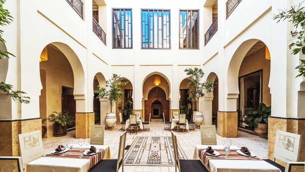 A hotel lobby with multiple dining tables, chairs, and potted plants. - Villa Makassar (Marrakech)