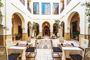 Eine Hotelhalle mit mehreren Esstischen, Stühlen und Topfpflanzen.