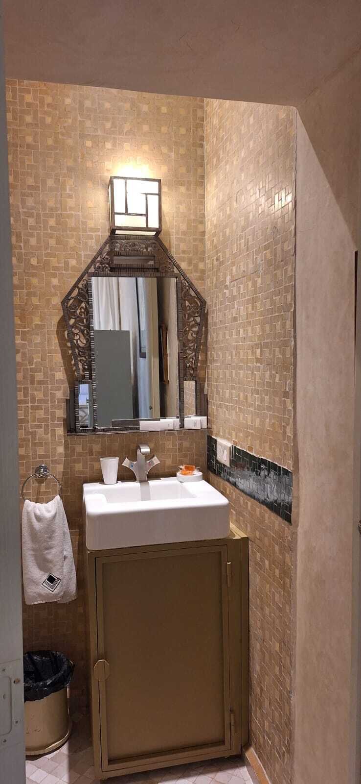 A bathroom with a tiled wall, a sink with a mirror above it, and a towel rack.