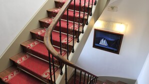 A spiral staircase with red carpeted steps and a wooden handrail. - Hôtel des Falaises (Etretat)