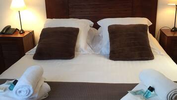 Una cama bien hecha con un cabecero marrón, dos almohadas y dos toallas enrolladas a un lado.