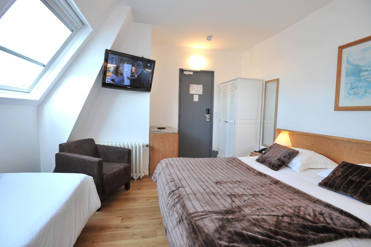 A hotel room with a bed, a chair, a TV mounted on the wall, a door, and a window.