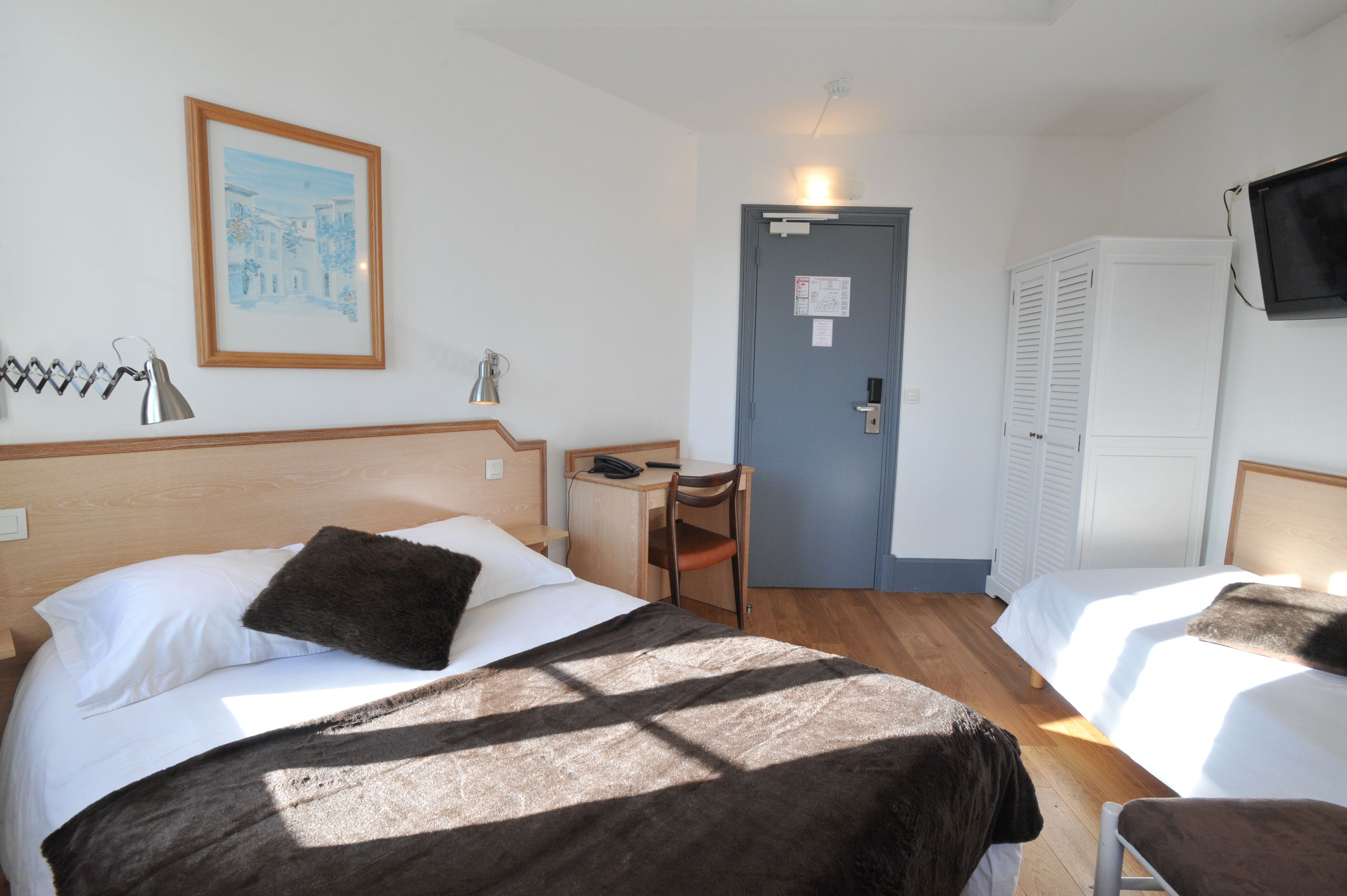 A hotel room with two beds, a desk, a chair, a TV, and a door.
