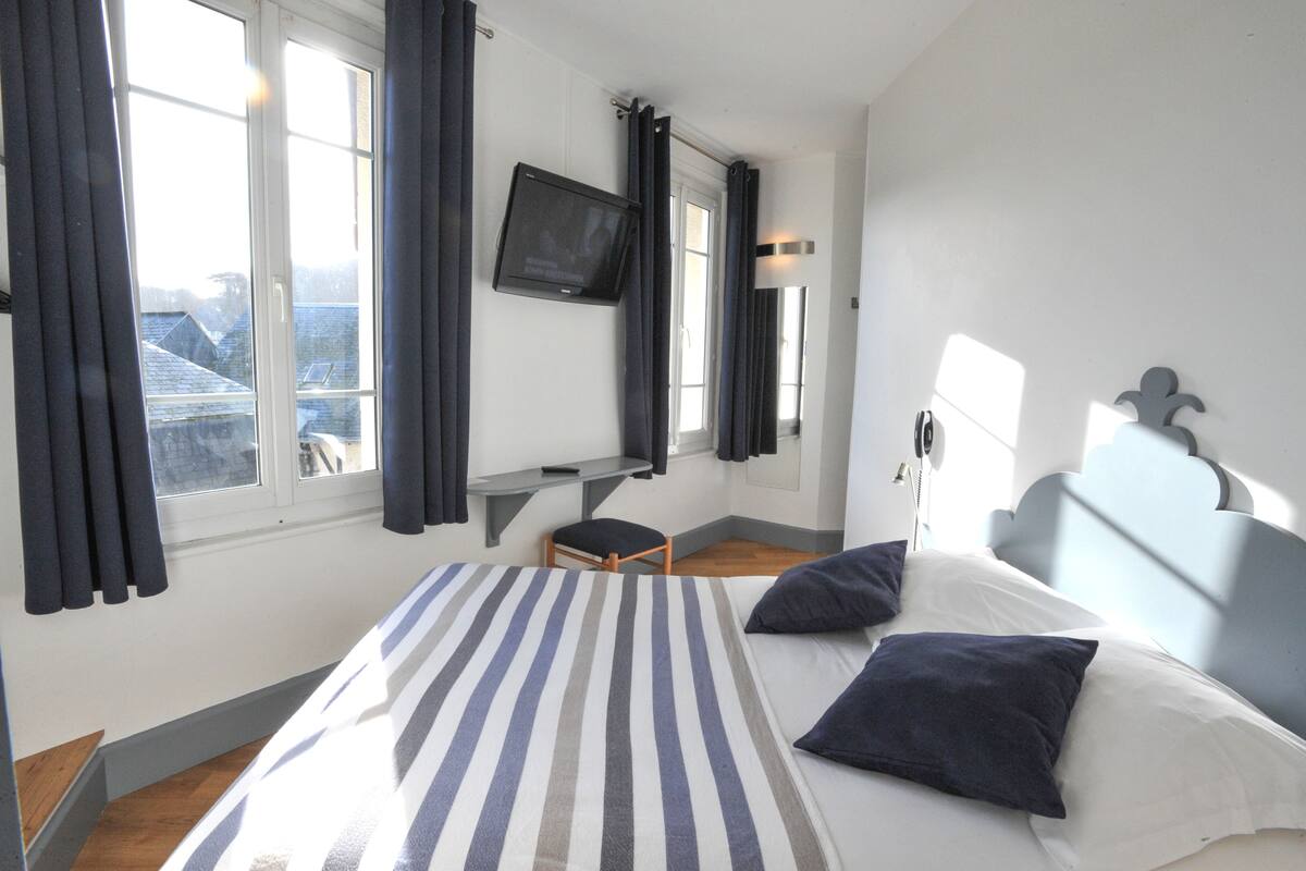 A hotel room with a bed, a desk, a chair, a TV, and a window with curtains.
