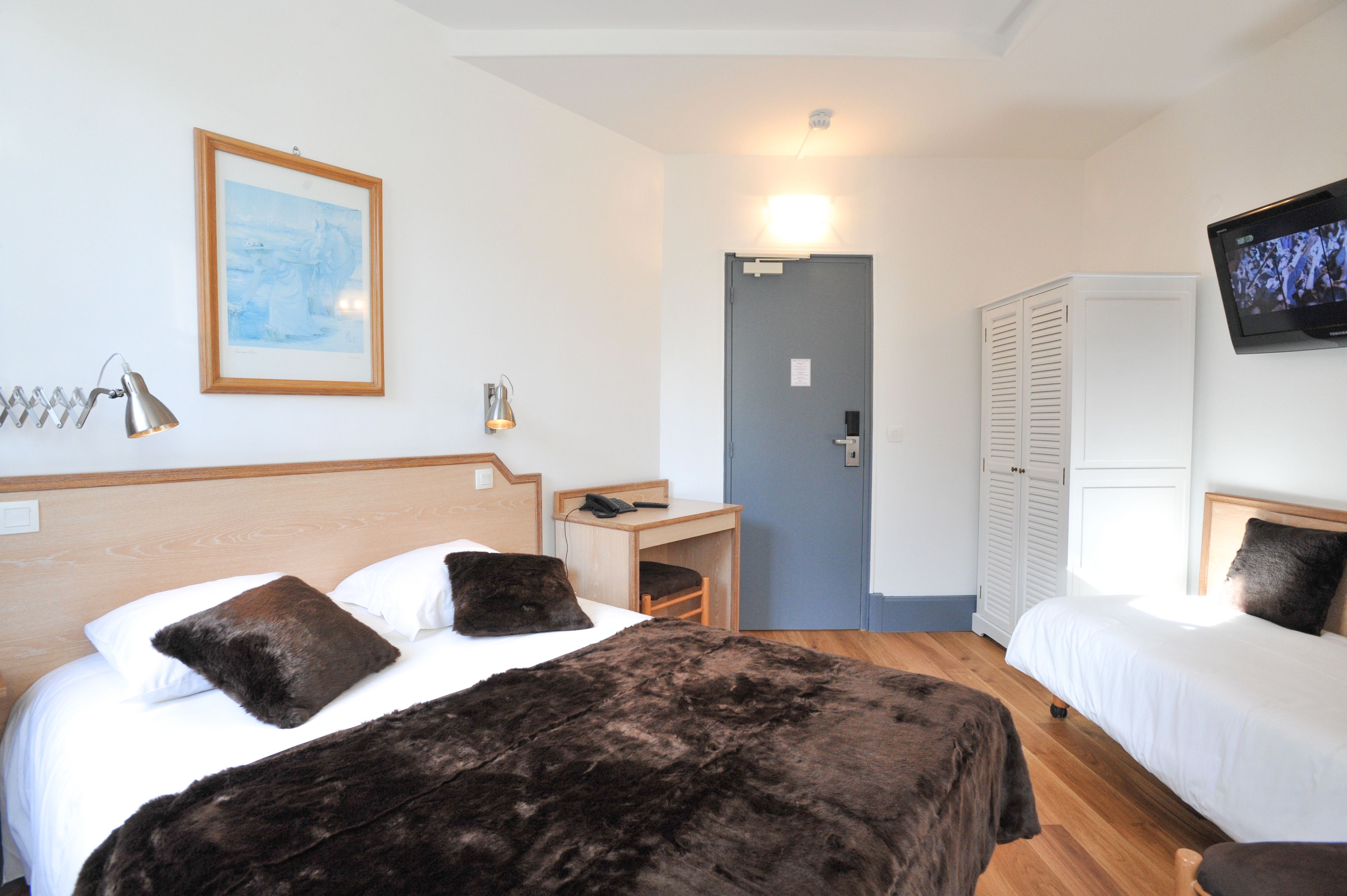 Une chambre d’hôtel avec deux lits, un bureau, une chaise, une télévision et une armoire.