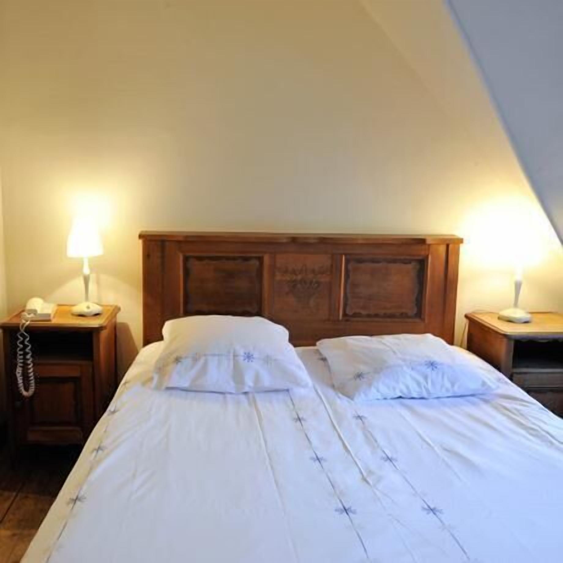 A single bed with a wooden headboard, two bedside tables with lamps, and a telephone on the left table.
