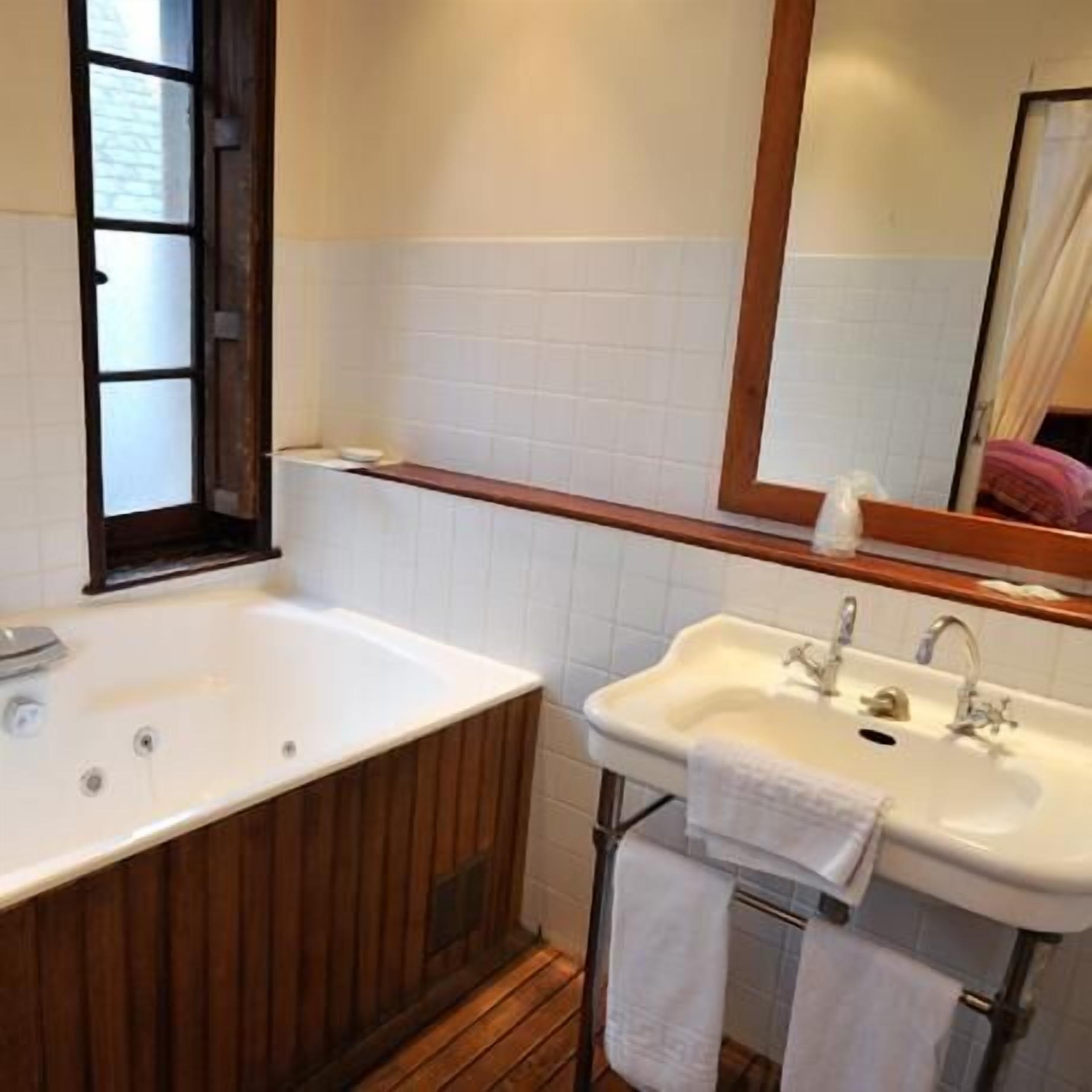 Une salle de bain avec une baignoire en bois, un lavabo blanc et un miroir au-dessus du lavabo.