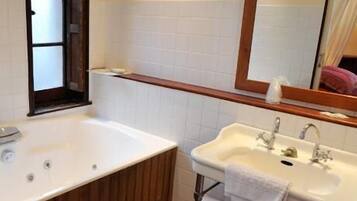 Une salle de bain avec une baignoire en bois, un lavabo blanc et un miroir au-dessus du lavabo.