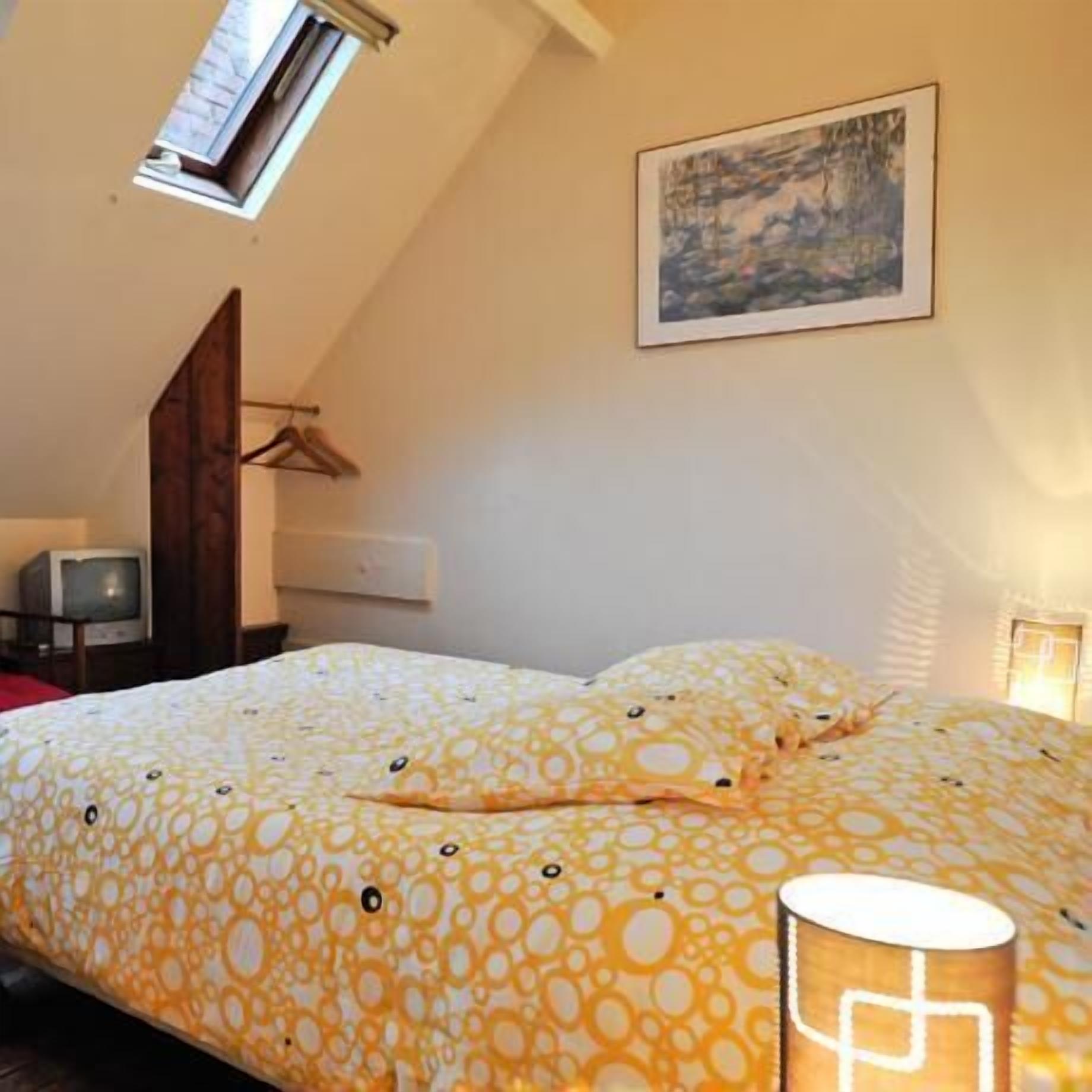 A bedroom with a bed, a TV, a painting, and a lamp.