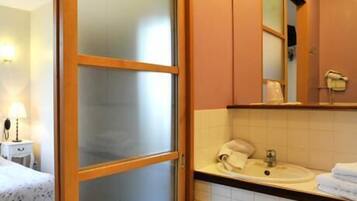 A hotel room with a bed, a bedside table with a lamp, a bathroom with a sink, a mirror, and a towel rack.