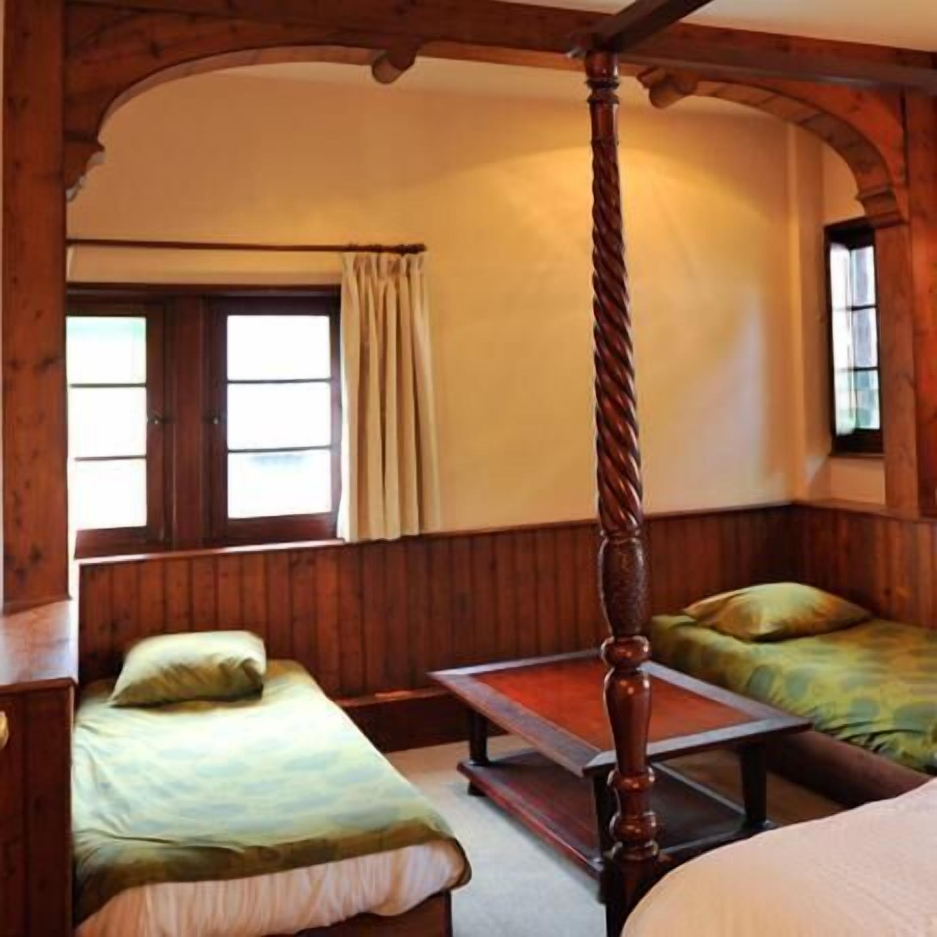 Una habitación con una cama con dosel, dos camas individuales, una mesa de madera y un ventanal con cortinas.