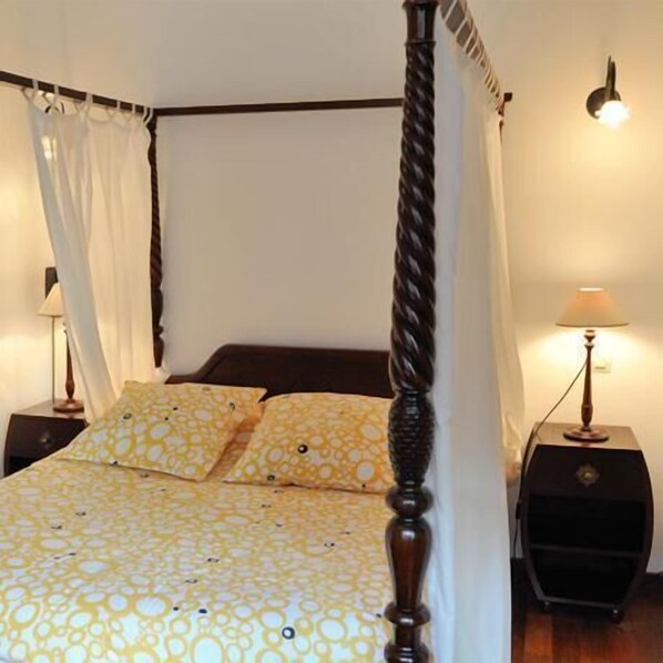 A four-poster bed with a canopy, a bedside table with a lamp, and a wall-mounted light fixture.