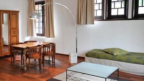A room with a wooden dining table and chairs, a sofa, a floor lamp, and a window with curtains. - Hôtel La Résidence Manoir de La Salamandre (Etretat)