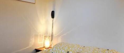 A bedroom with a bed, a nightstand, a wall-mounted lamp, and a framed picture on the wall.