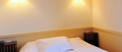 A neatly made bed with white linens in a hotel room.