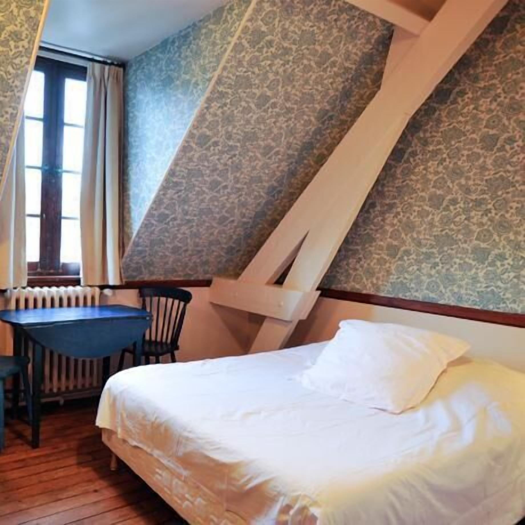 Ein Schlafzimmer mit schrägen Wänden, einem Bett, einem Tisch und einem Stuhl.