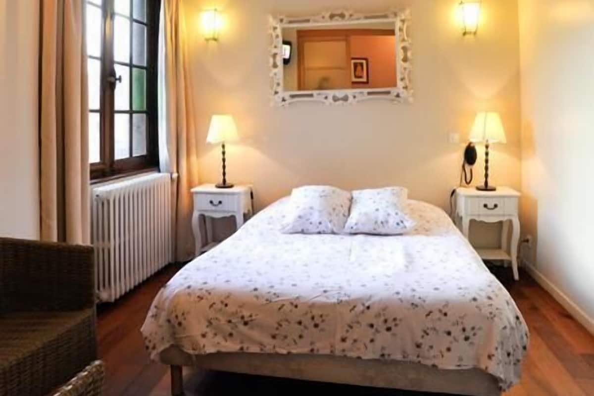 A bedroom with a bed, two bedside tables with lamps, a mirror above the bed, and a window with curtains.