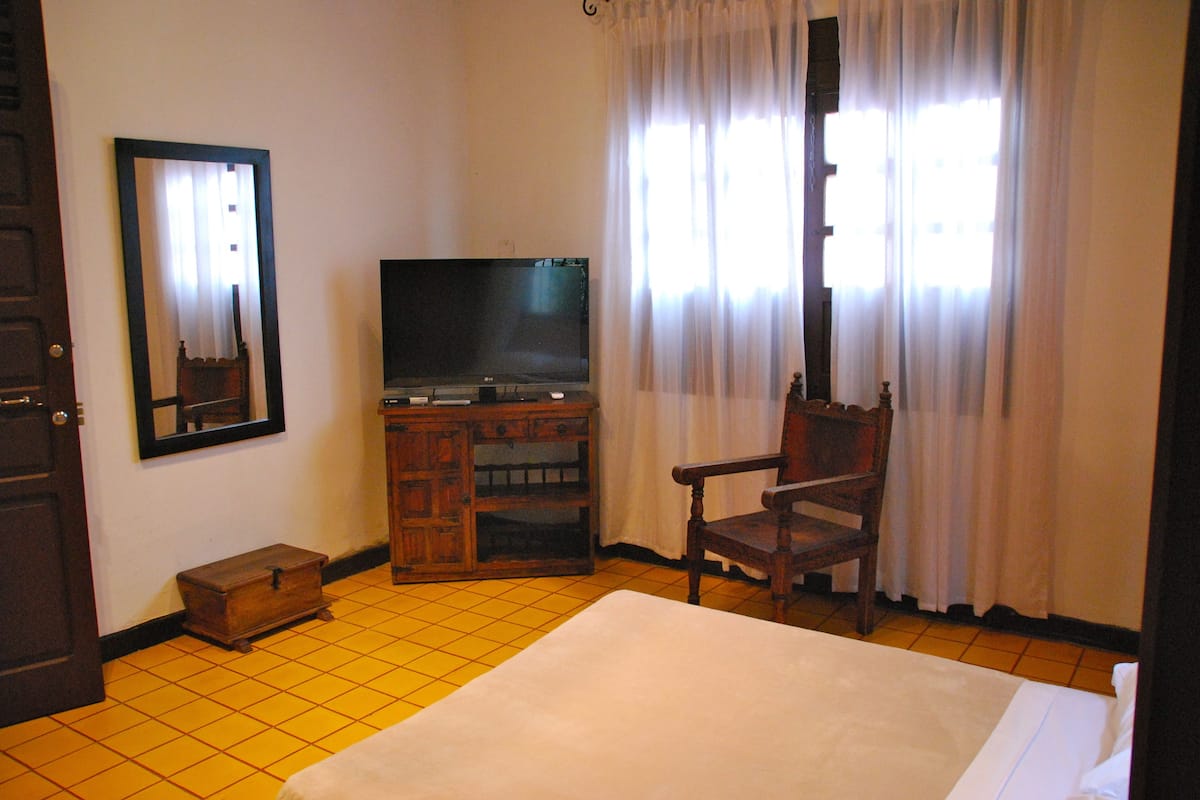 Una habitación de hotel con una cama, televisión, armario de madera, silla y un espejo en la pared.