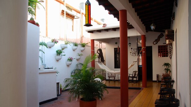 A narrow corridor with tiled flooring, white walls, and red pillars. There are potted plants along the walls and a hammock in the center. - Hotel Del Parque (Santa Marta)