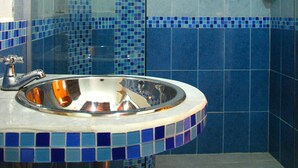 A bathroom with a glass shower enclosure, a sink with a blue-tiled countertop, and blue-tiled walls. - Hotel Del Parque (Santa Marta)