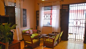A room with a tiled floor, a sofa with cushions, two wooden chairs, a small table, and a potted plant. - Hotel Del Parque (Santa Marta)