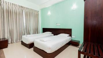A hotel room with two beds, a wooden headboard, a wooden bench, and a curtain.