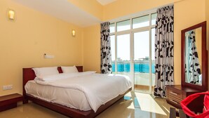 A hotel room with a large bed, a wooden nightstand, a red chair, and a view of the sea through the balcony. - Supun Arcade Residency (Colombo)