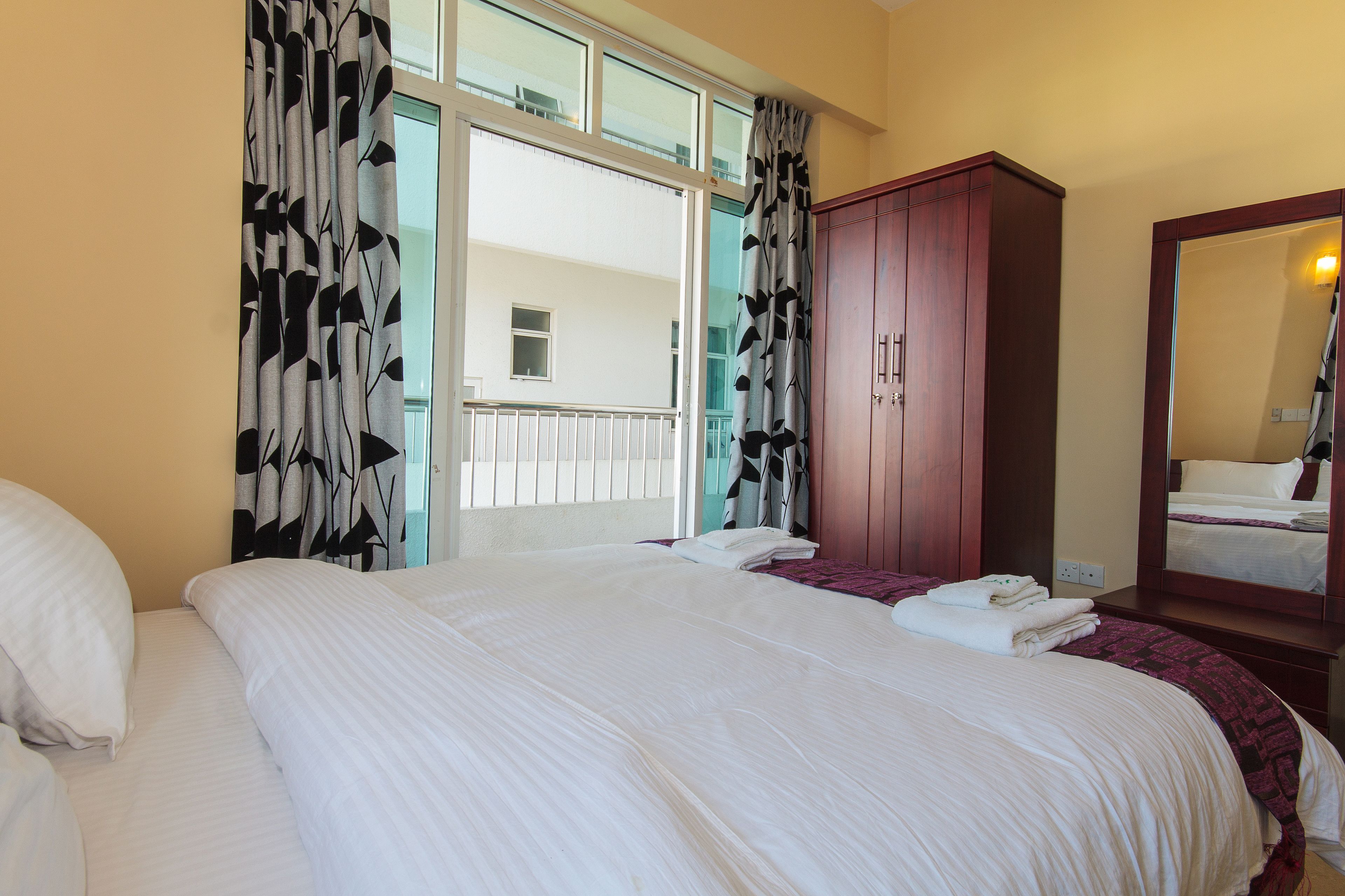 Habitació d'hotel amb un llit gran, un armari, un mirall i una finestra amb cortines.