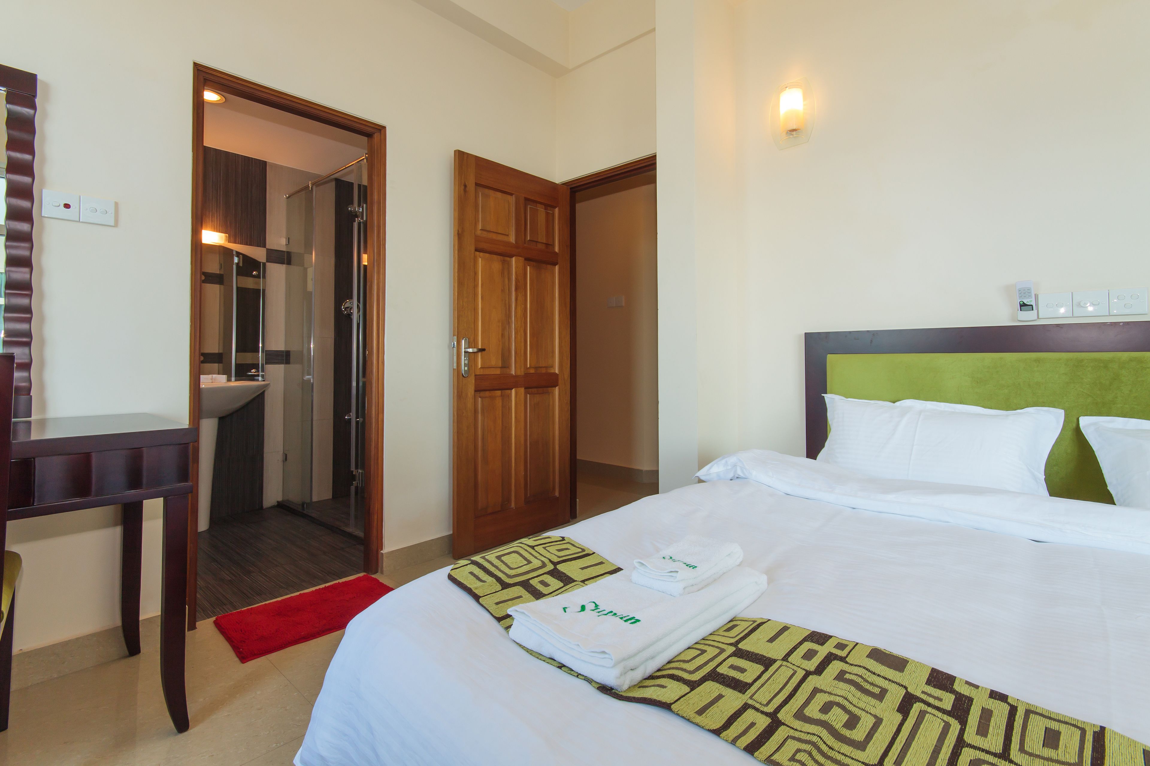 Una habitación de hotel con cama, escritorio, zona de ducha y puerta que da a otra habitación.