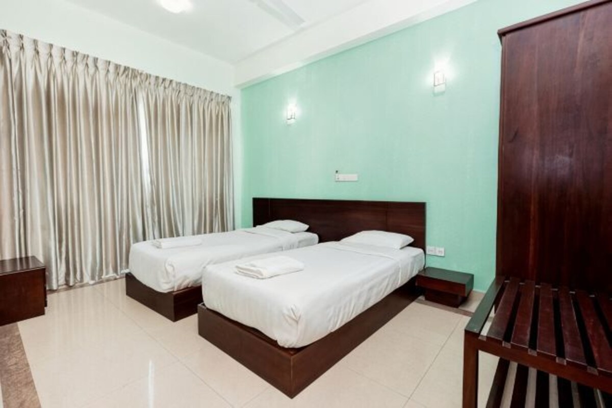 A hotel room with two beds, a wooden wardrobe, a nightstand, and a window with curtains.