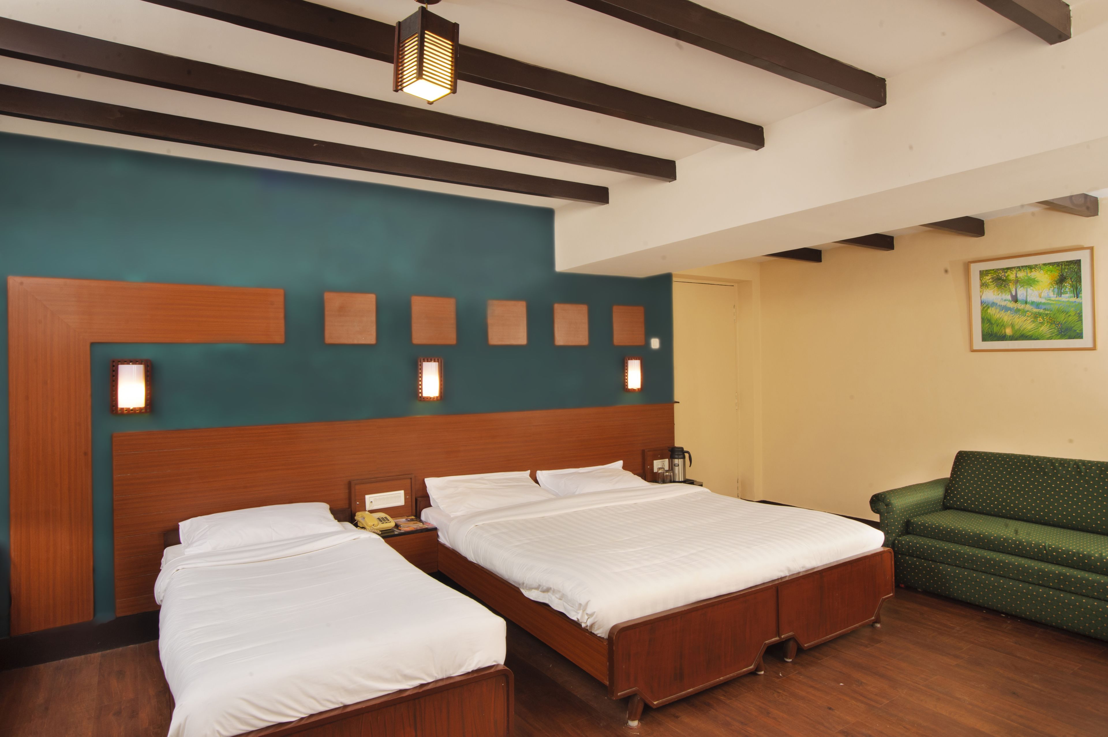 Une chambre d’hôtel avec deux lits, un canapé vert, une tête de lit en bois, des murs de couleur turquoise et un tableau.