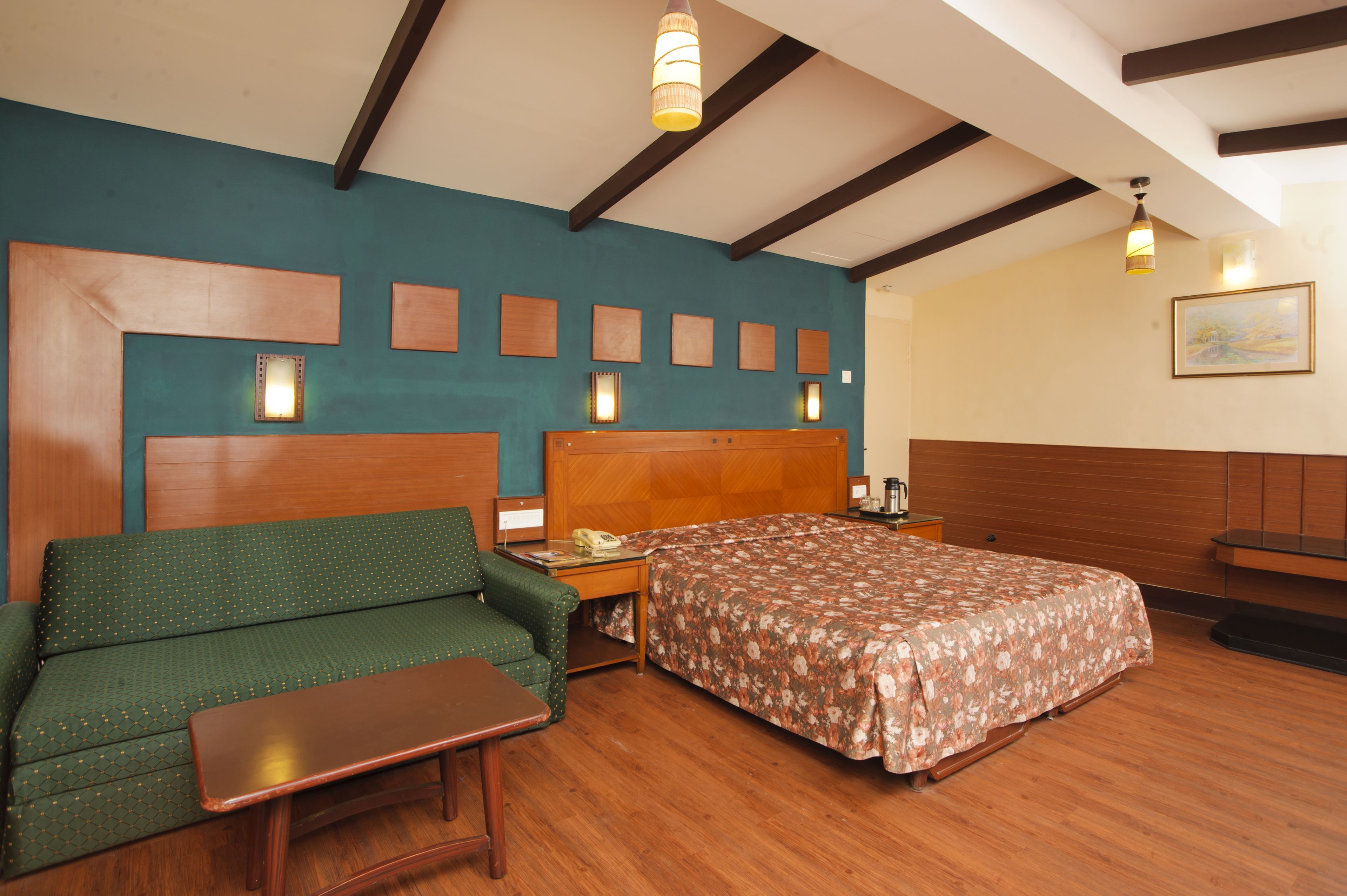 Una habitación de hotel con un cabecero de madera, un sofá verde, una cama de madera y una mesita.