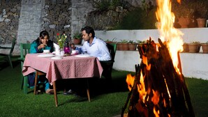 A dining table with a checkered tablecloth, surrounded by chairs, with a fire in the background. - Hotel Jai (Kodaikanal)