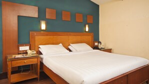A neatly made bed with white linens, a wooden headboard, and two bedside tables with lamps. - Hotel Jai (Kodaikanal)