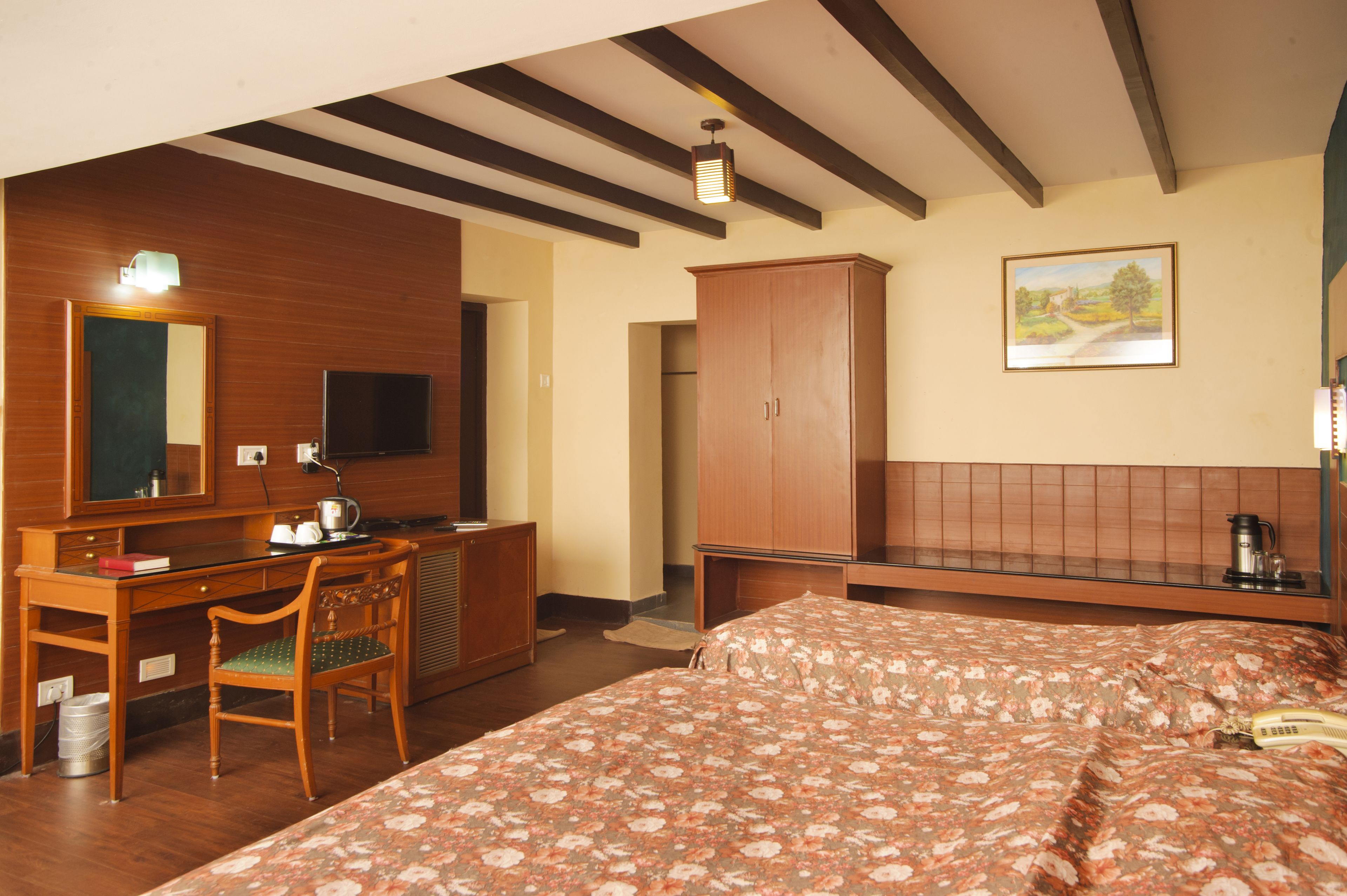 Een hotelkamer met een houten bureau, een bed met bloemenbedrukking, een kledingkast en een schilderij aan de muur.