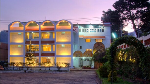 A multi-story hotel with a central courtyard, featuring a well-lit entrance and a landscaped garden. - Hotel Jai (Kodaikanal)