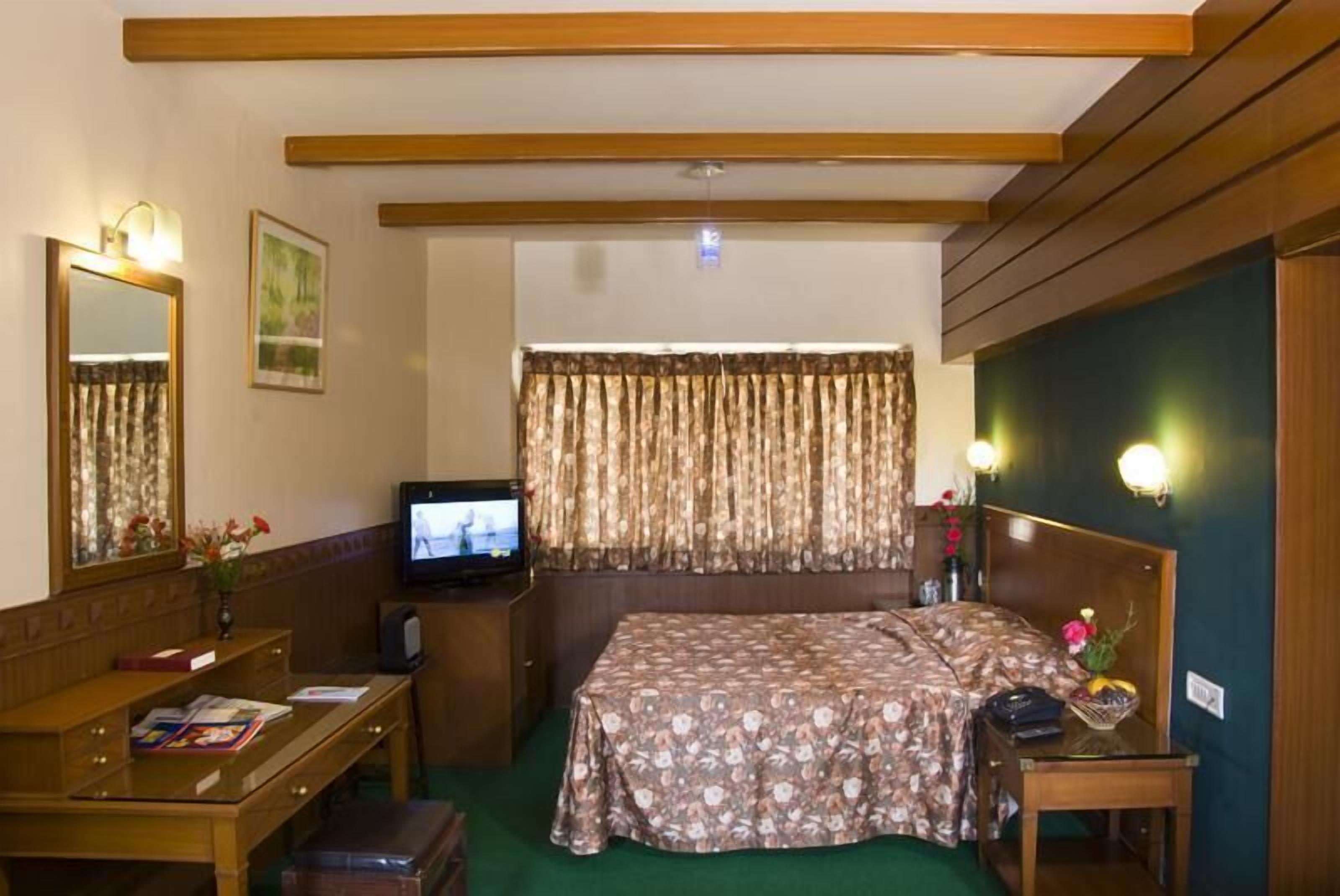 A hotel room with a bed, a desk with a chair, a television, and a mirror.